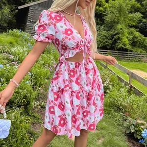 Robe d'été rose à fleurs avec décolleté en V, découpes à la taille et ourlet volanté