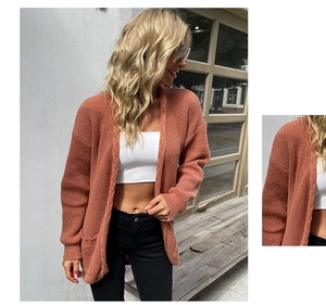 Detail of rust red knitted cardigan showing textured cable knit fabric and side pockets