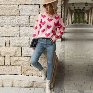 Detail shot of pink knit sweater featuring dark pink heart patterns and crew neck design
