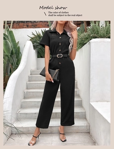 Detail of short sleeve black jumpsuit with lace shoulder trim and gold buckle belt