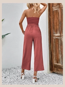 Back view of a dusty rose strapless wide-leg jumpsuit with shirred bust and belt detail