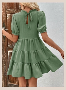 Back view of sage green tiered dress featuring bow tie neck and ruffled hem details