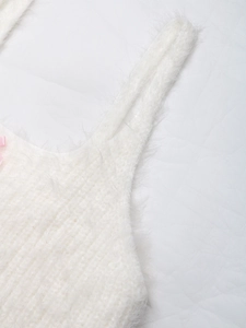 Dettaglio ravvicinato del top in maglia bianca con un delicato fiocco rosa in seta