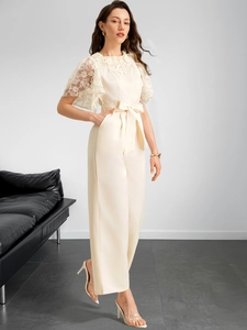 Detail of lace embroidery on white jumpsuit with ruffled sleeves and waist tie