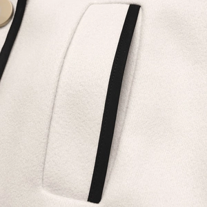Detailed macro view of cream wool coat pockets with black contrast piping and gold button