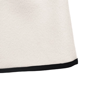 Detailed close-up of thick white wool coat texture with contrast black piping edges