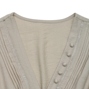 Detail of V-neckline with pleats, lace inserts, and fabric buttons on beige dress