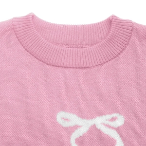 Close-up of pink knit sweater featuring a white bow jacquard pattern and ribbed neckline