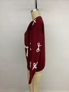Detail of red knit cardigan featuring white bow patterns and ribbed cuff finishing