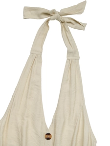 Dettaglio tuta beige con scollo a V, bottone marmorizzato e fiocco decorativo