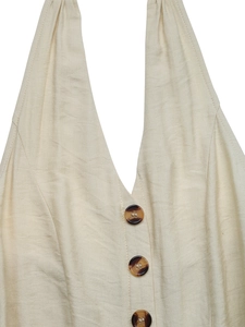 Dettaglio di tuta beige allacciata al collo con scollo a V e bottoni tartarugati
