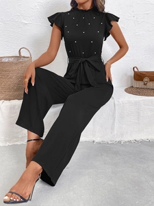 Detail of ruffled stand collar and white pearl beads on a black high-waisted jumpsuit