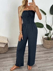 Detail of smocked strapless jumpsuit in dark blue textured fabric with bow tie neck