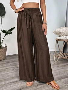 Detail of dark brown wide-leg trousers with elastic drawstring waist and textured fabric