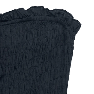 Close-up of black smocked fabric texture with elastic shirring and ruffle trim detail