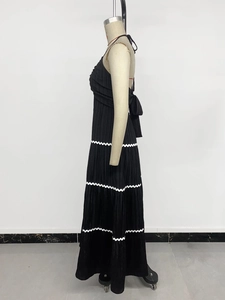 Close-up of black pleated maxi dress showing white wavy lace details and back bow design
