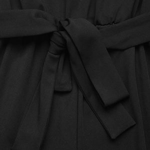 Detail of waist-tie design on a black high-waisted jumpsuit with natural fabric drapes