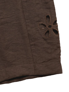 Macro detail of embroidered flower cutout on brown wide-leg trousers fabric