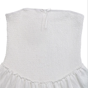 Detailed view of white smocked tube top with delicate ribbon bow and ruffled hemline