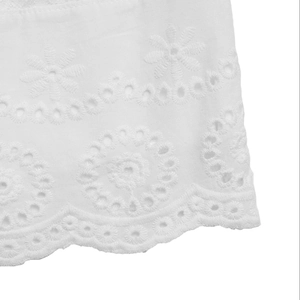 Close-up of white dress showing intricate floral eyelet embroidery and scalloped hem details