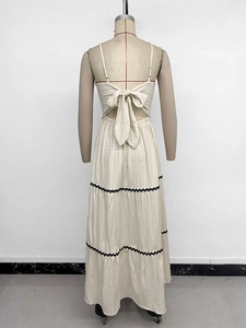 Detail of tiered beige maxi dress featuring back bow tie and black wavy lace trim
