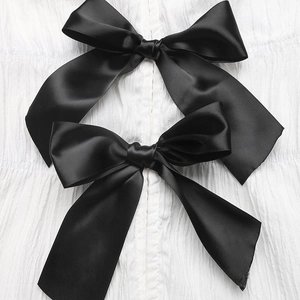 Close-up of black satin bows on white textured pleated fabric of an elegant summer shirt