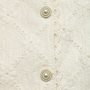 Detail of elegant cream lace blouse with embossed floral texture and pearl gold buttons