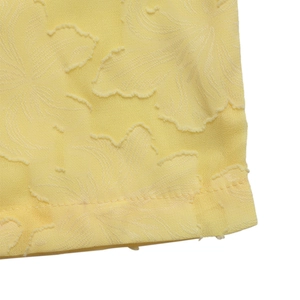 Détail macro du tissu jacquard jaune pâle montrant la texture florale et l'ourlet piqué