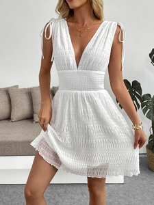 Detailed view of white V-neck dress with smocked waist and textured fabric detail