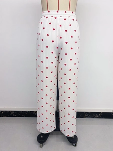 Dettaglio dei pantaloni bianchi a gamba larga con motivi a cuore rosso ed elastico