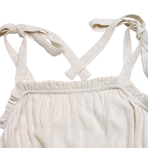 Dettaglio dello scollo a punto smock e spalline regolabili sulla tutina color crema in lino