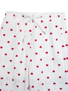 Dettaglio dei pantaloni larghi bianchi con motivi a cuore rosso e vita con coulisse