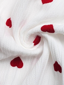 Dettaglio del tessuto bianco stropicciato con piccole stampe a cuore rosso dei pantaloni