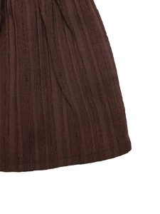 Detail shot of deep brown dress hem showing vertical pleated texture and stitched edges