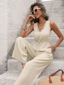 Detail of cream sleeveless textured jumpsuit featuring button front and drawstring waist
