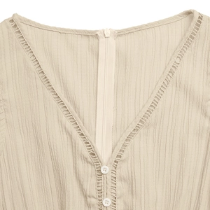 Detail of V-neckline with delicate lace trim and button on beige textured jumpsuit