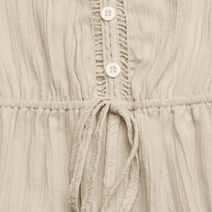 Detail shot of beige textured jumpsuit featuring a button placket and lace crochet trim