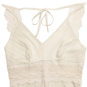 Close-up of pleated beige V-neck dress featuring delicate lace trim and neck tie detail
