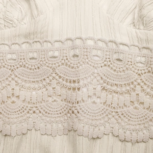 Close-up of beige summer dress featuring delicate crochet lace stitching and pleated fabric
