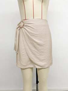 Detail of beige wrap mini skirt featuring a metallic ring buckle and textured fabric