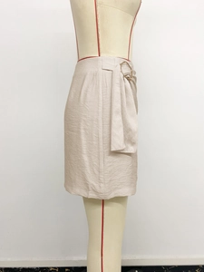 Detail view of high-waist beige skirt featuring golden metal buckle and belt detail