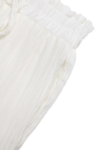 Detail of white pleated fabric showing elastic waistband and stitching on trousers