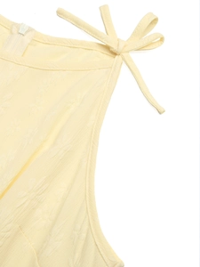 Detail of cream sleeveless jumpsuit featuring bow shoulder ties and floral jacquard fabric