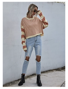 Detail van een gestreepte gebreide trui met oranje banden en trendy distressed jeans