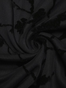 Macro shot of black mesh fabric featuring elegant floral flocking texture and soft draping
