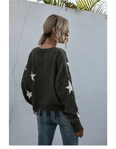 Close-up of charcoal knit sweater featuring white star patterns and distressed tassel hem