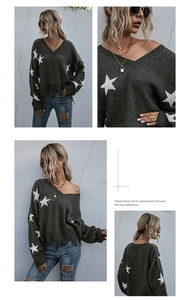 Close-up of distressed fringe hem and white star patterns on grey v-neck knit sweater