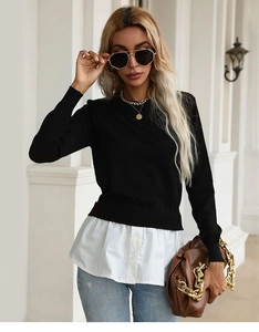 Detail view of women's black knit sweater with white shirt hem layered design