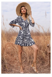 Detail of V-neck summer dress with white leaf print on navy blue fabric in outdoor setting