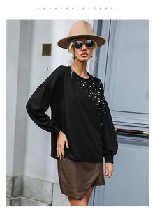 Detail of white pearls embellishment on black loose knit top with crew neck